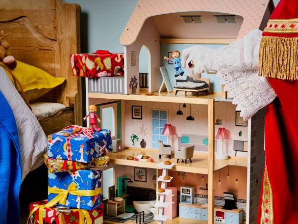 Sinterklaas legt cadeautjes bij een houten poppenhuis en een bed.