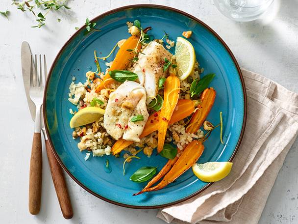 Witte vis, geroosterde wortels en rijst op een blauw bord.