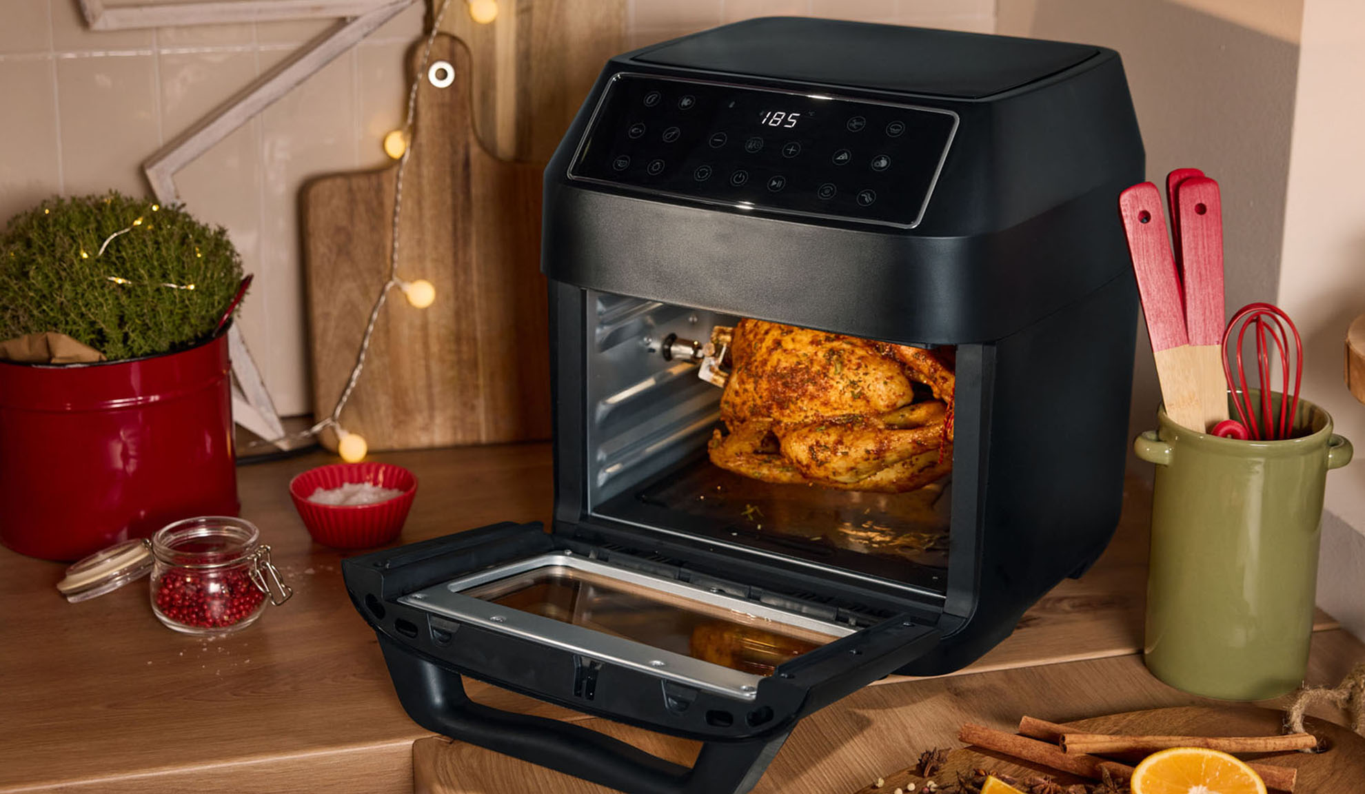 Airfryer met gebraden kip, kruiden en kerstdecoraties in de keuken.