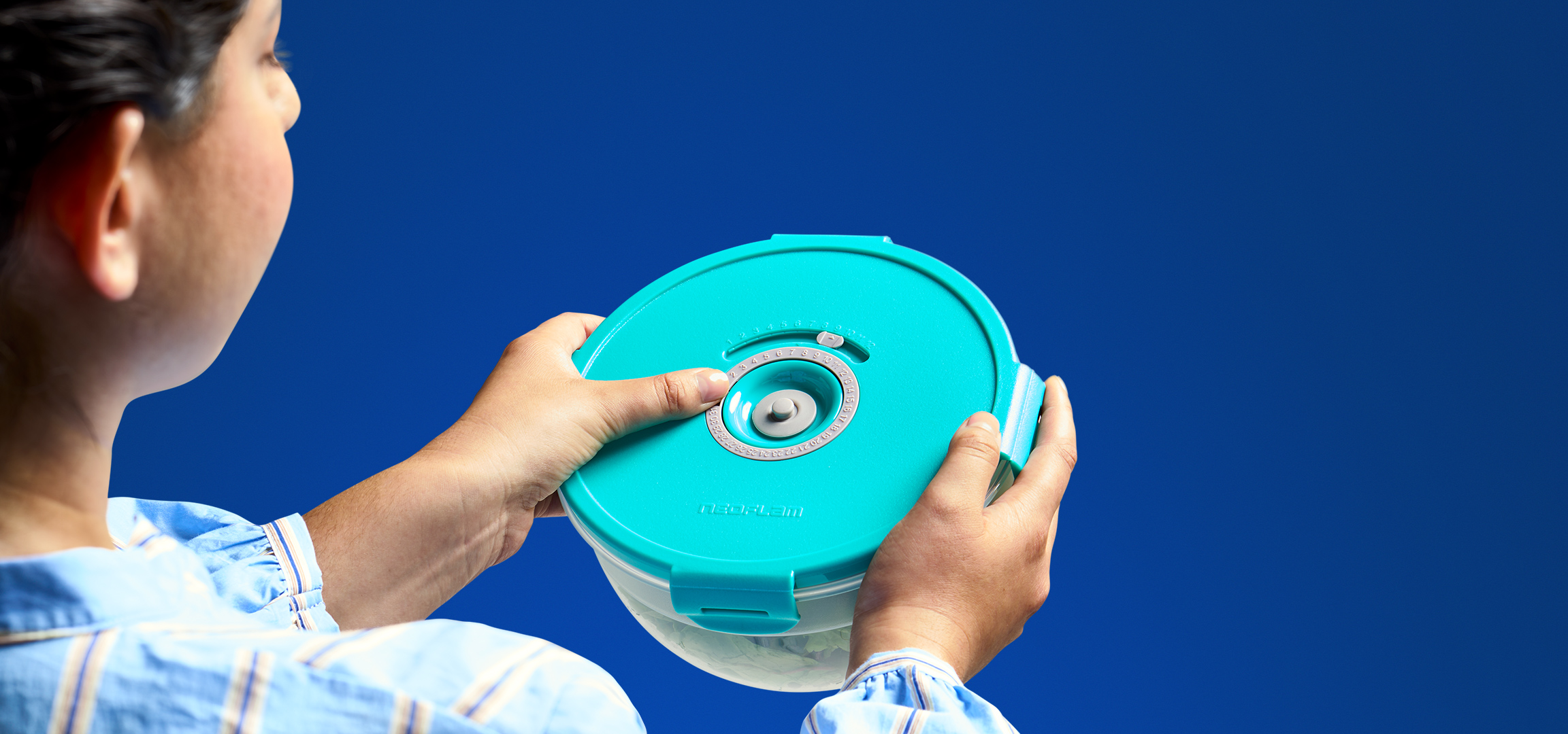 Een persoon die een turquoise voedselcontainer met een draaischijf voor datumaanduiding vasthoudt.