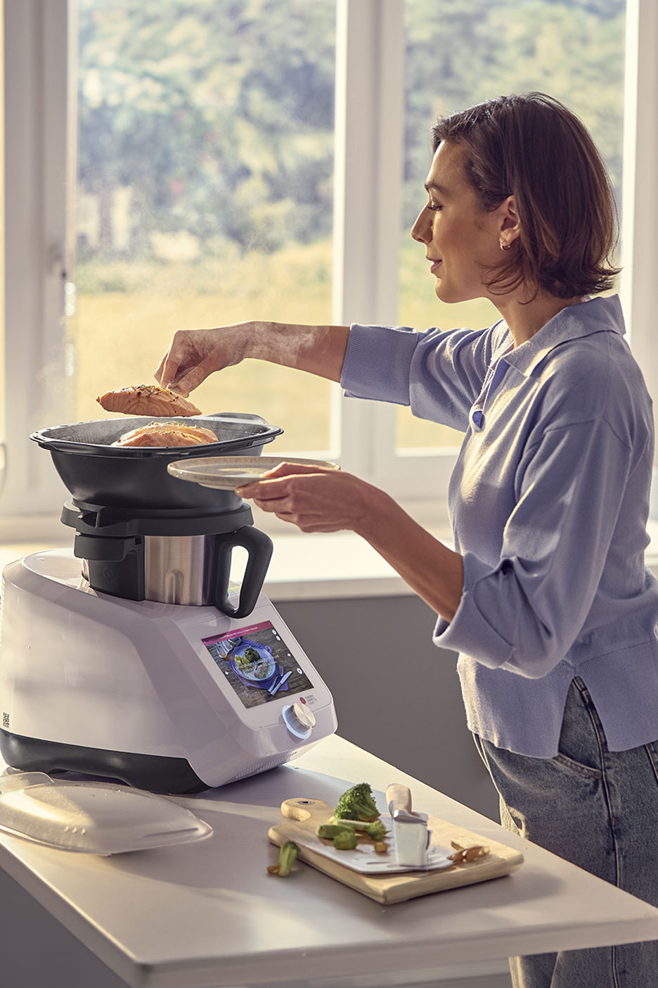 Vrouw bereidt zalm en groenten met een multifunctionele keukenmachine.