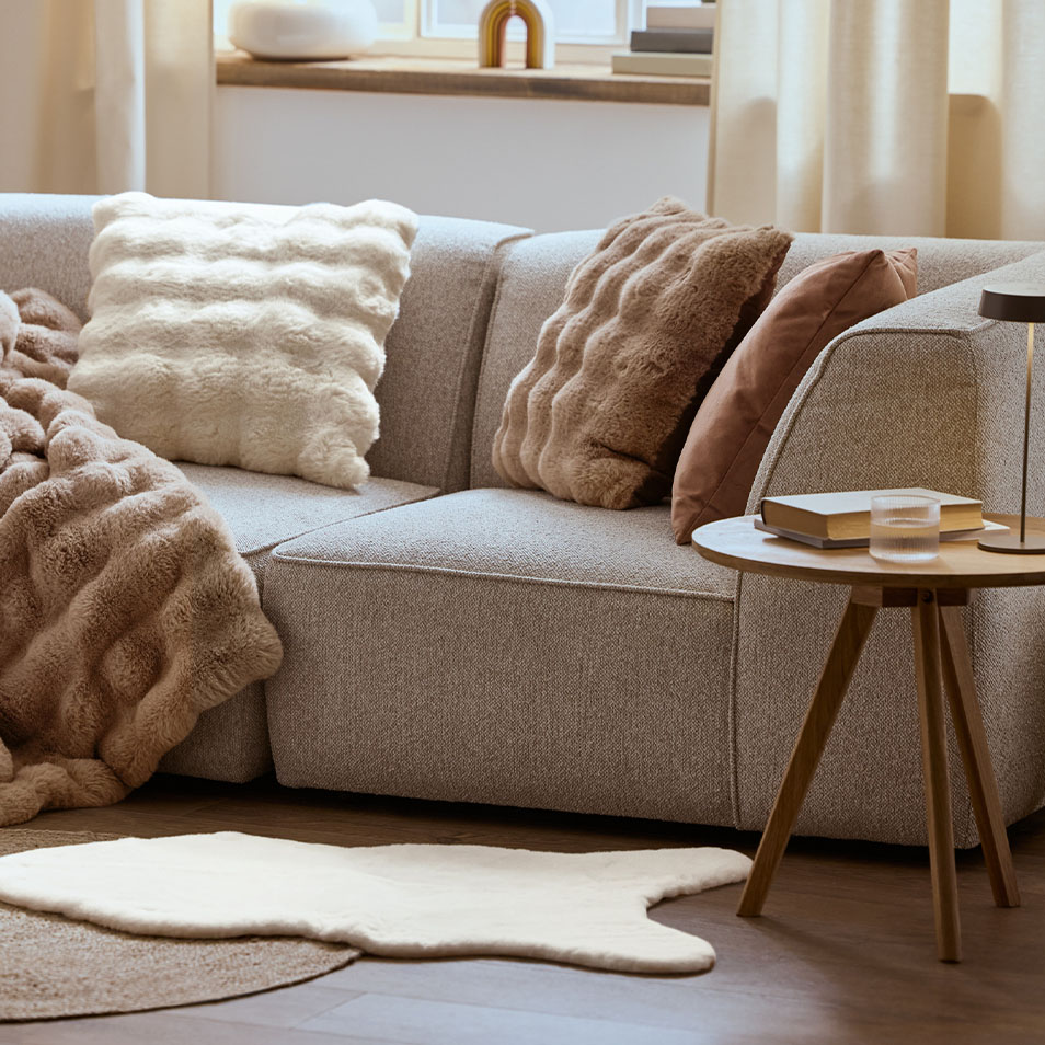 Grijze modulaire bank met pluizige kussens en plaids, naast een salontafel.