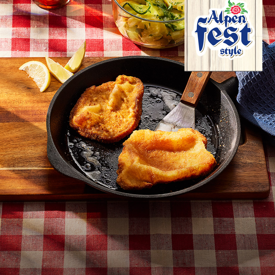 Twee gebakken schnitzels in een pan met citroenpartjes en een salade, met een 'Alpen Fest style' logo.