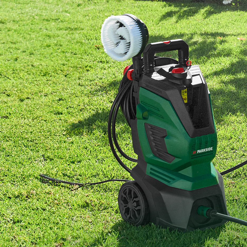 Hogedrukreiniger met roterende wasborstel op een groen gazon.