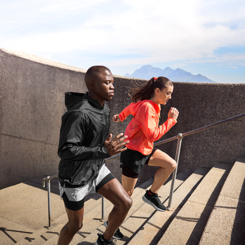 Twee sporters rennen een trap op, gekleed in sportjacks en shorts.