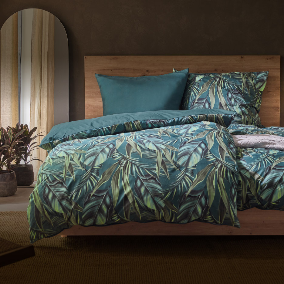 Bed met dekbedovertrek en kussensloop met tropisch bladmotief in groen en blauw.
