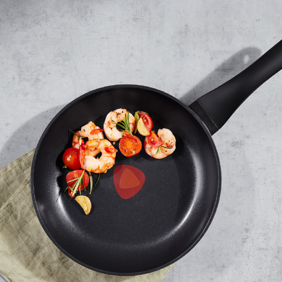 Garnalen en cherrytomaten in een zwarte koekenpan op een grijze ondergrond.