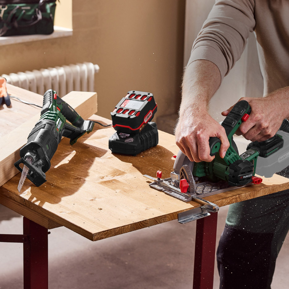 Een man zaagt hout met een cirkelzaag, met een reciprozaag en een werklamp op de achtergrond.