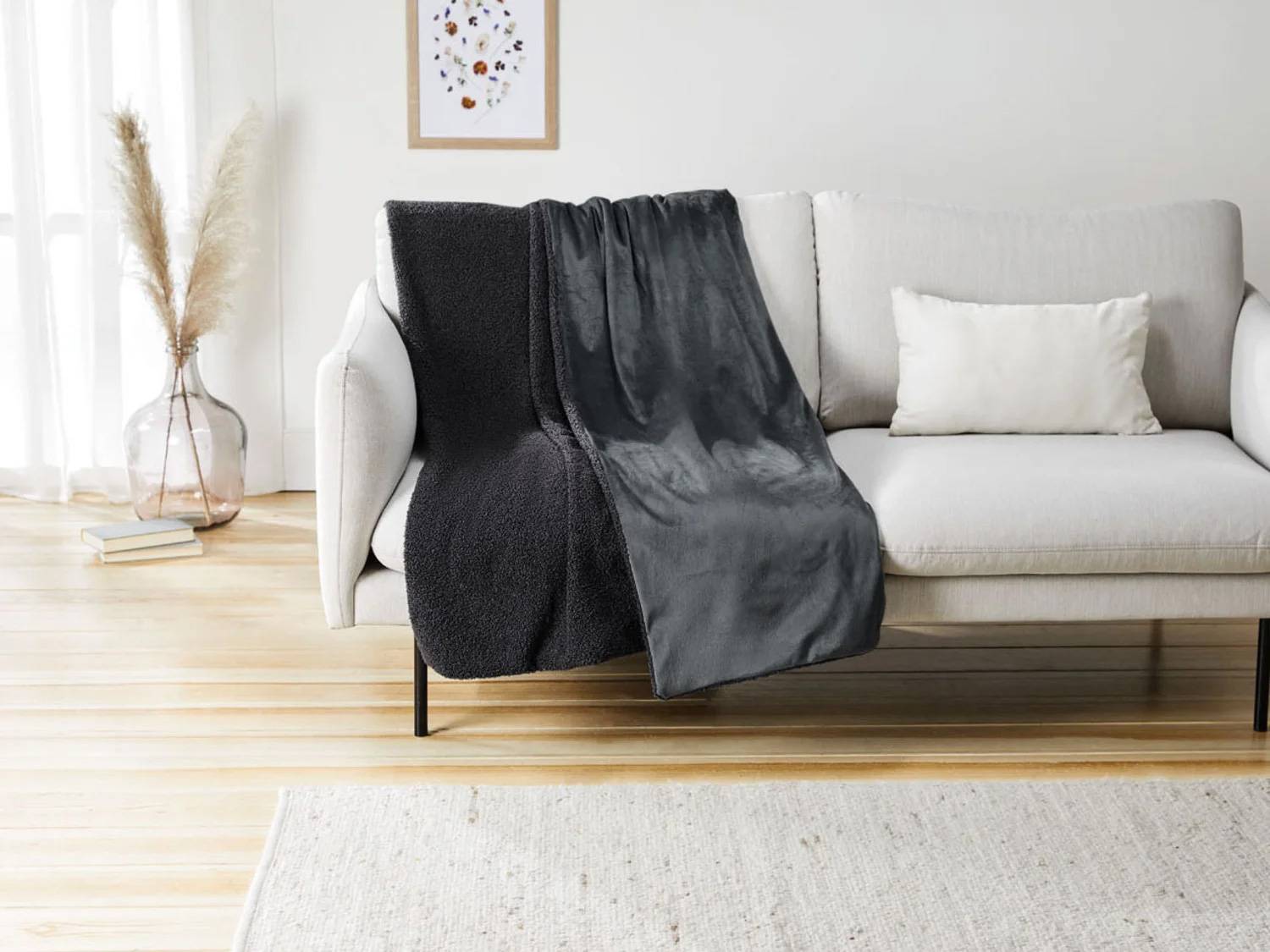 Een grijze bank met een donkergrijze deken en een wit kussen in een woonkamer.